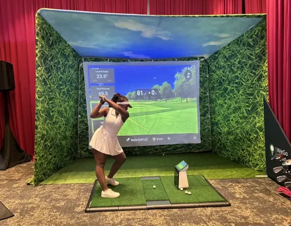 Golfer swinging from the hitting mat in front of a projected golf course inside a simulator enclosure